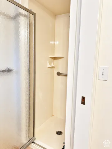 Shower enclosure with a textured glass door, integrated corner shelf, and a grab bar