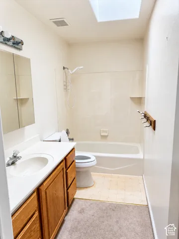Bathroom featuring a skylight, a single vanity with wood-finish cabinetry, a white countertop, and an integrated shower-tub combination