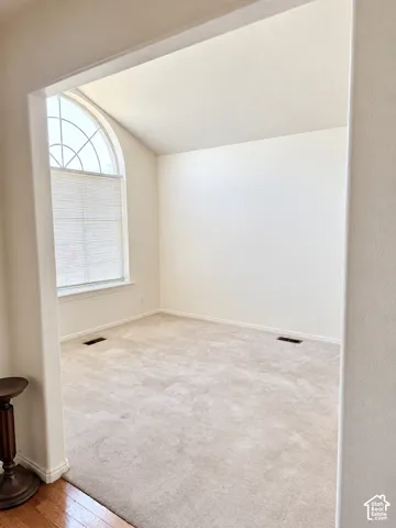 Vaulted ceiling room with an arched window, light-toned carpet, and a white wall finish