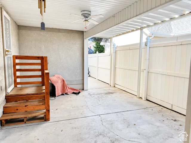 Covered patio area featuring a ceiling fan, concrete flooring, stucco exterior wall, and privacy fencing