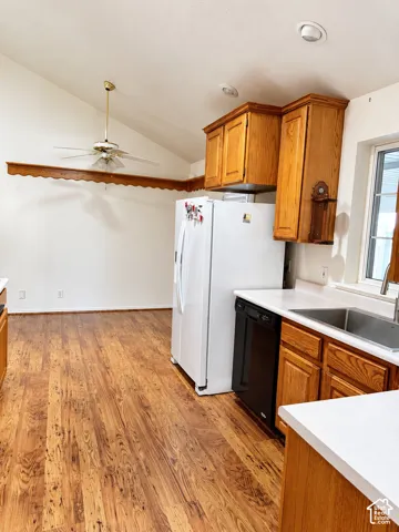 Vaulted ceiling with a ceiling fan, wood-finish flooring, wood cabinetry, white countertops, and stainless-steel sink