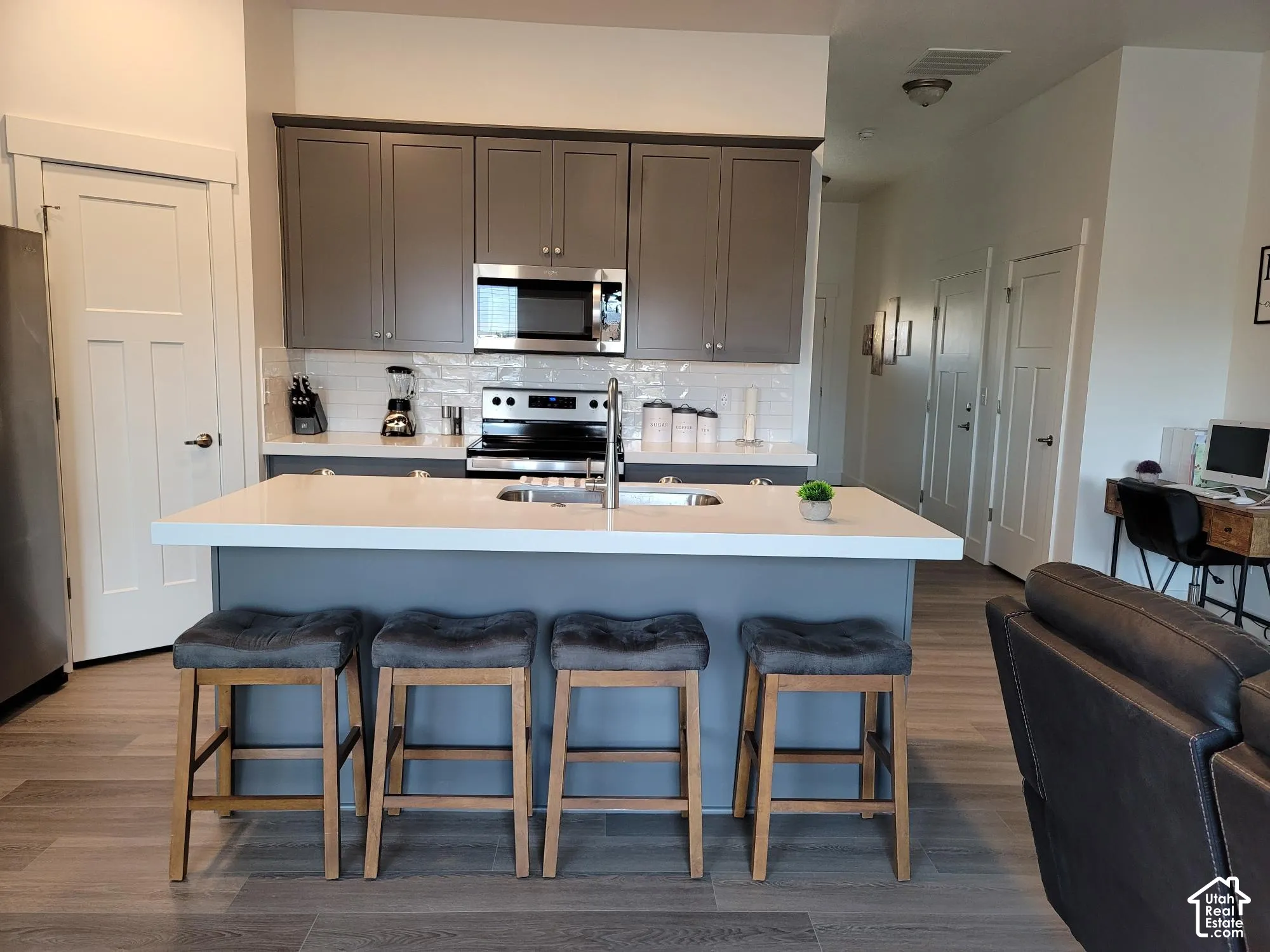 Modern kitchen featuring gray cabinetry, stainless steel appliances, white subway tile backsplash, and an island with an undermount sink