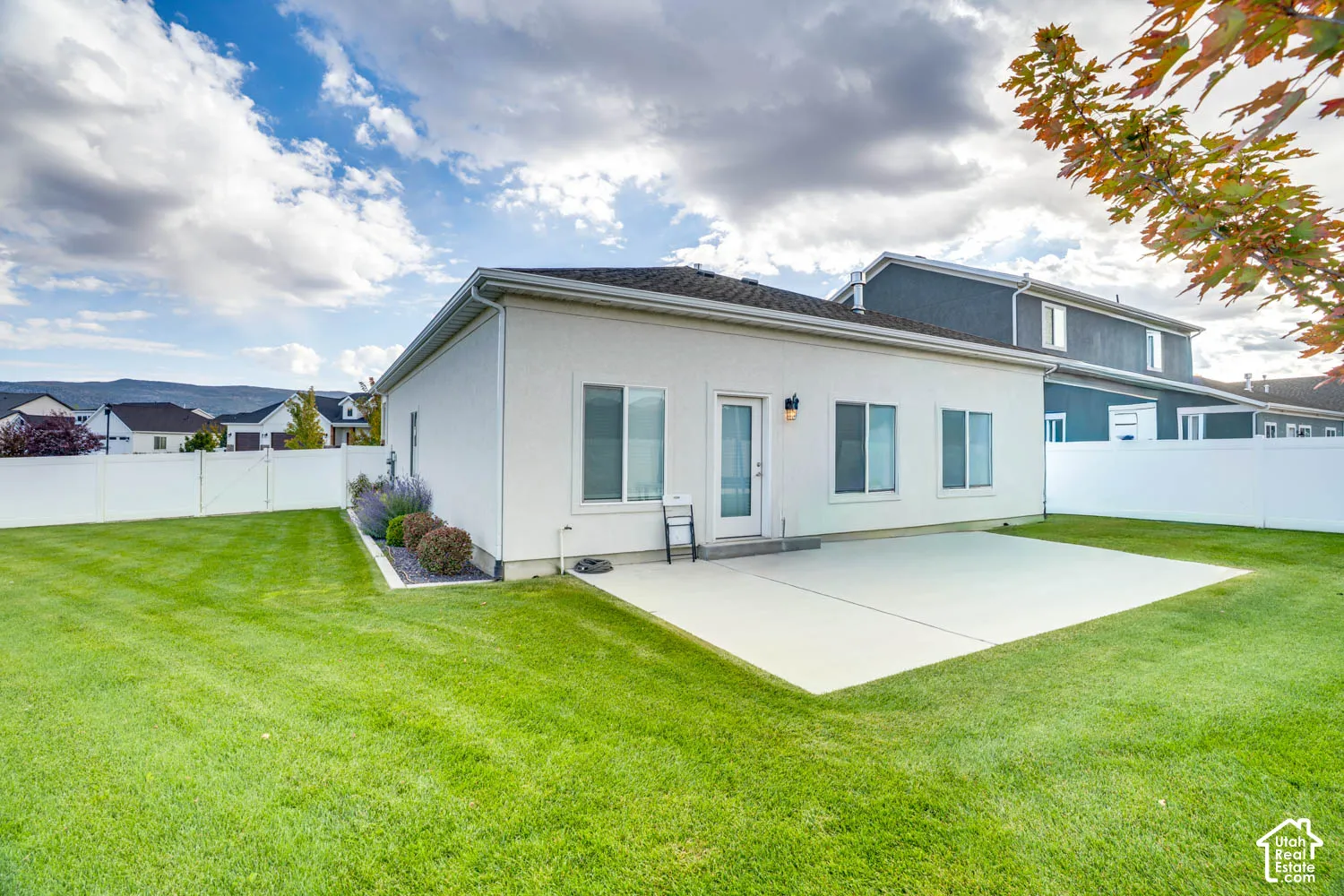 Expansive rear lawn, privacy fencing, concrete patio, and exterior lighting