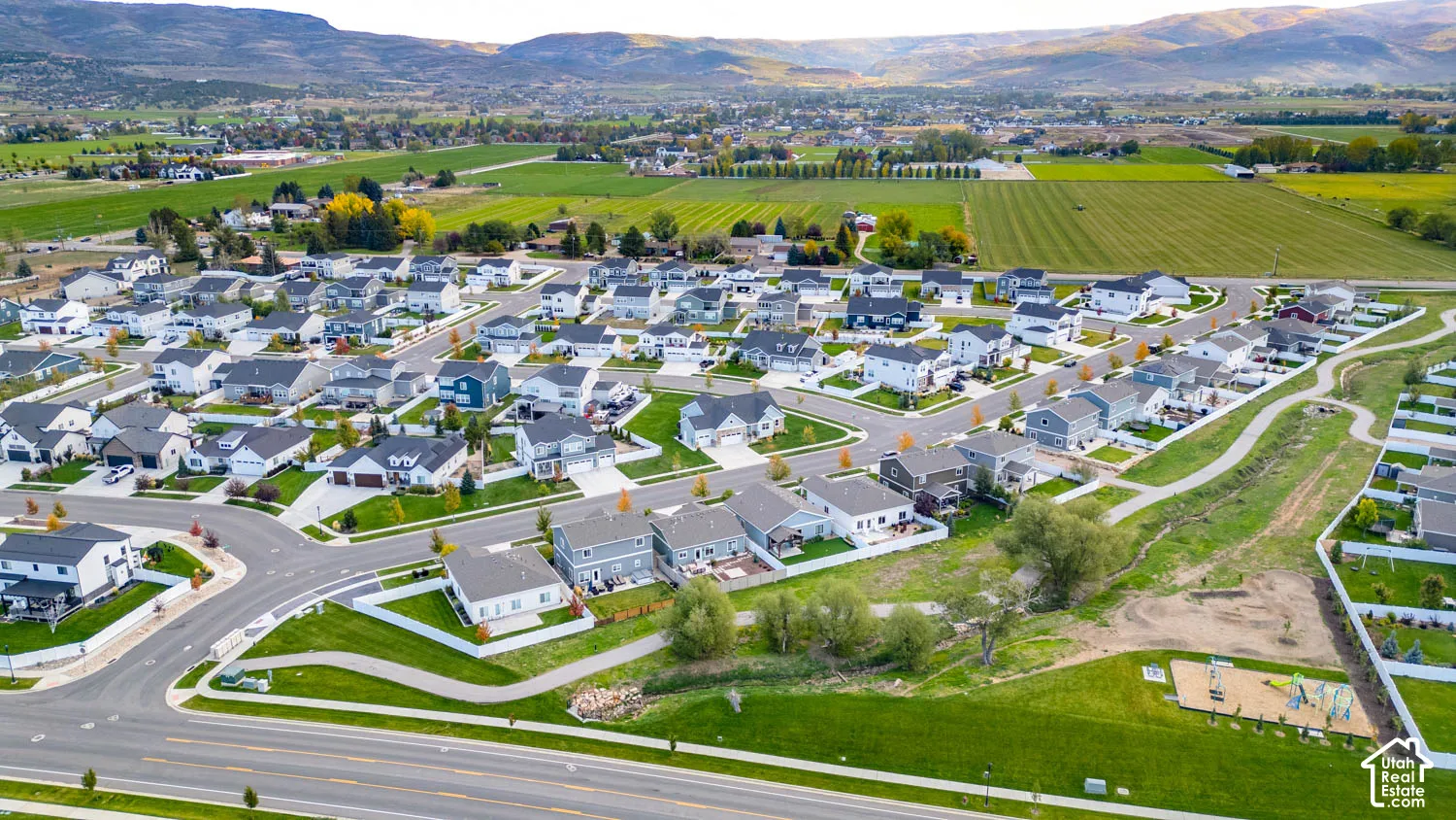 New construction residential development with varied home exteriors, mountain backdrop, paved roadways, and green spaces