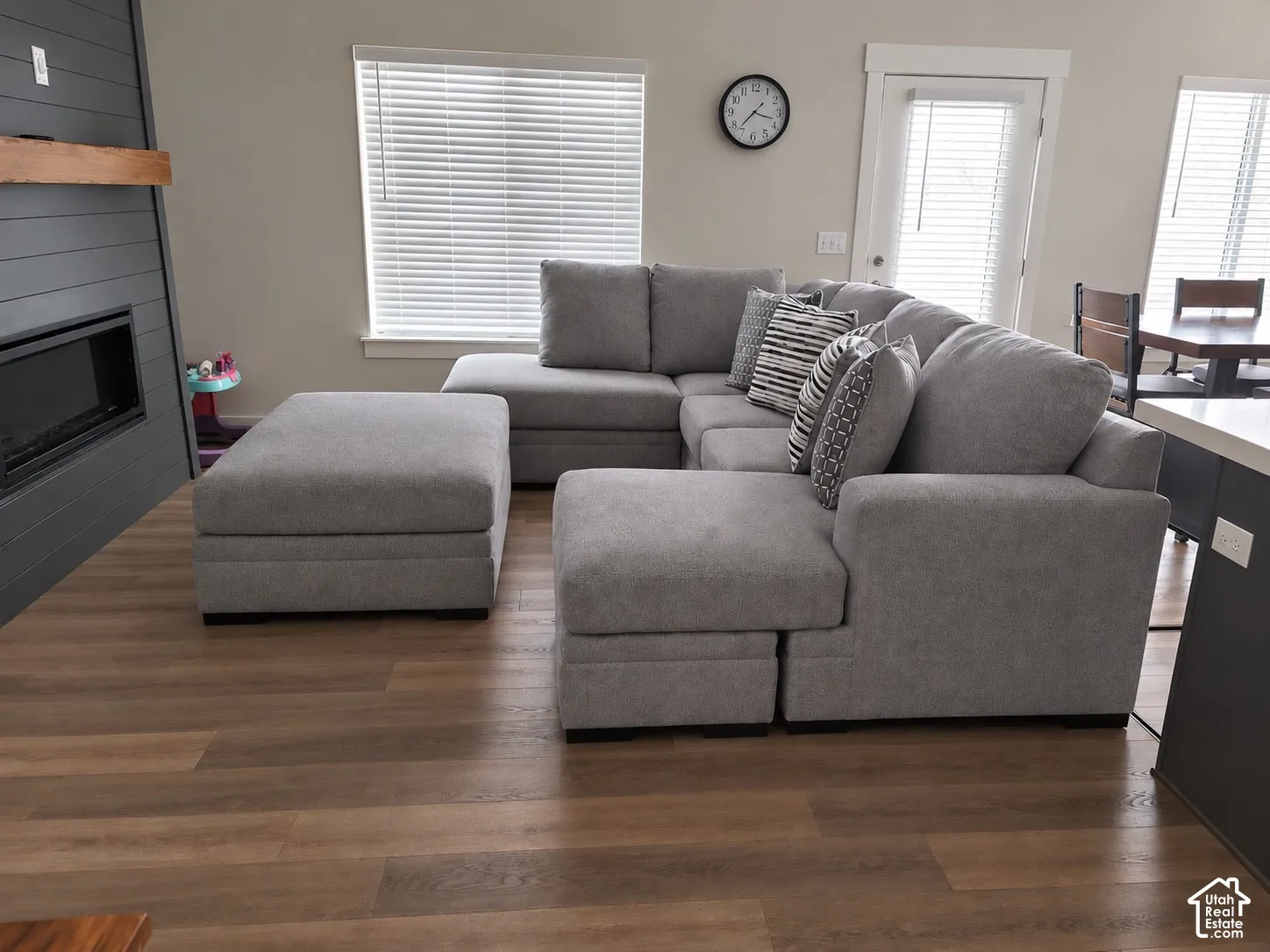 Modern living area featuring wood-finish flooring, a contemporary fireplace with a dark shiplap surround, and a light wood mantel