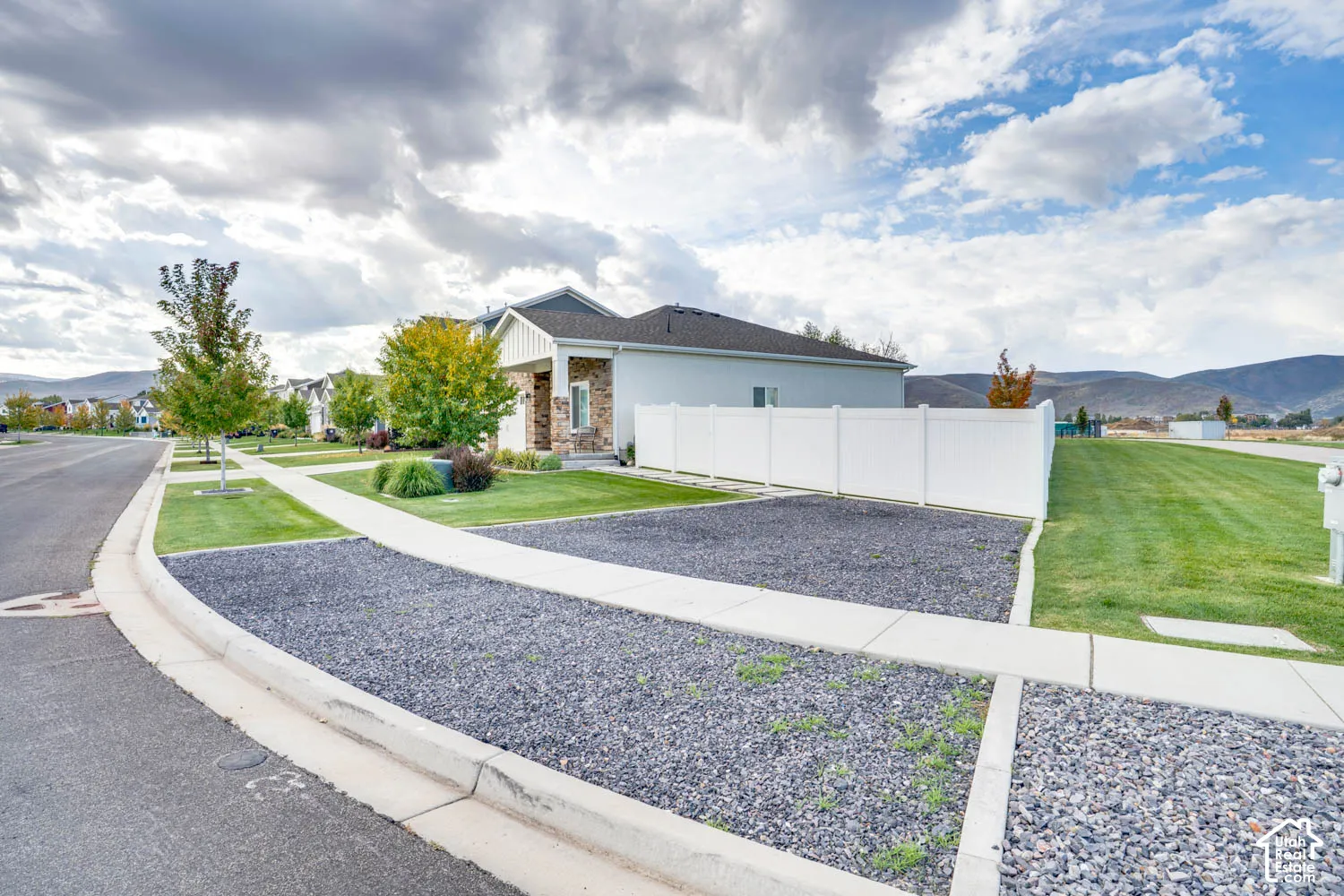 Contemporary residence featuring a covered porch with stone detailing, a white privacy fence, and a landscaped yard with mature trees