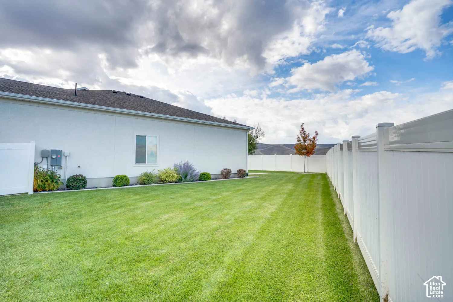 Expansive green lawn with a white vinyl fence, mature landscaping, and a stucco exterior