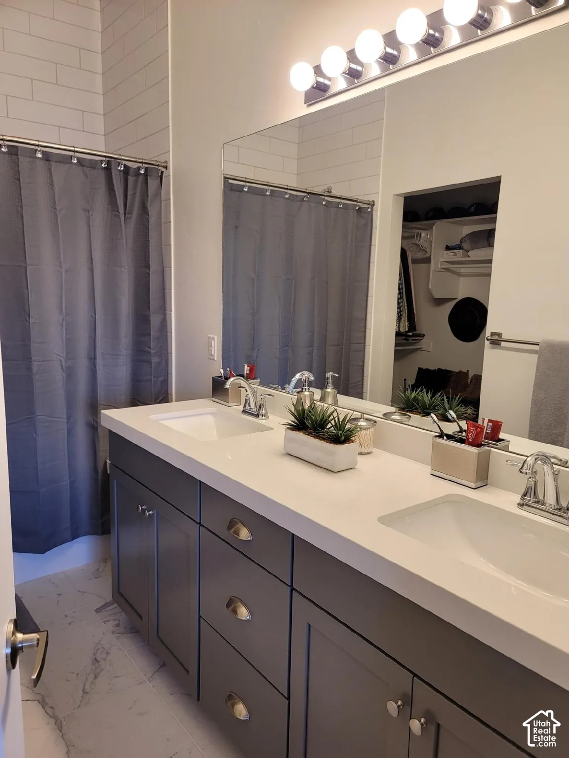 Double vanity with integrated sinks, white countertop, gray cabinetry, subway tile shower surround, and large wall mirror