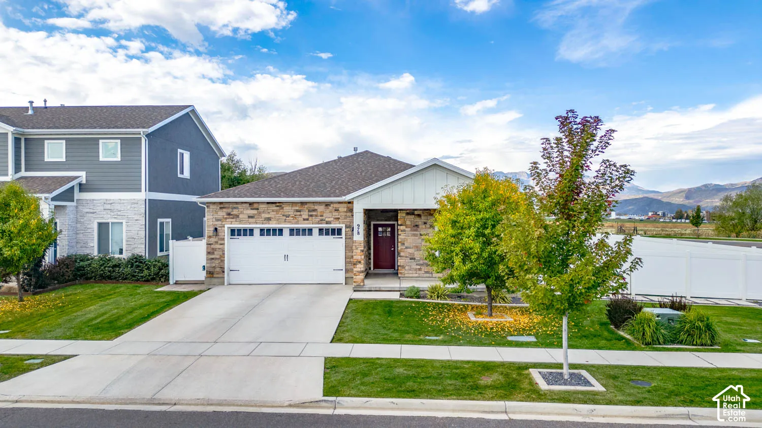 Stone-clad exterior, attached two-car garage, concrete driveway, red entry door, and manicured landscaping