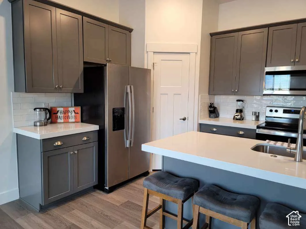 Kitchen featuring gray shaker-style cabinetry, white countertops, stainless steel appliances, and wood-finish flooring