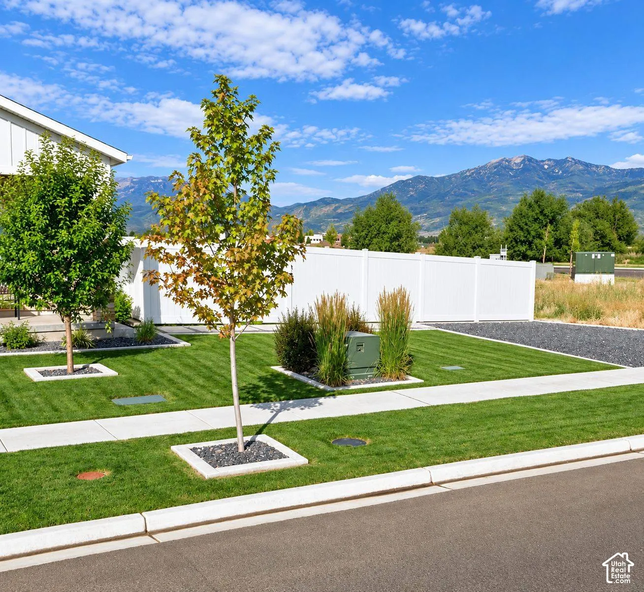 Manicured lawn with mature trees, white privacy fencing, and mountain scenery