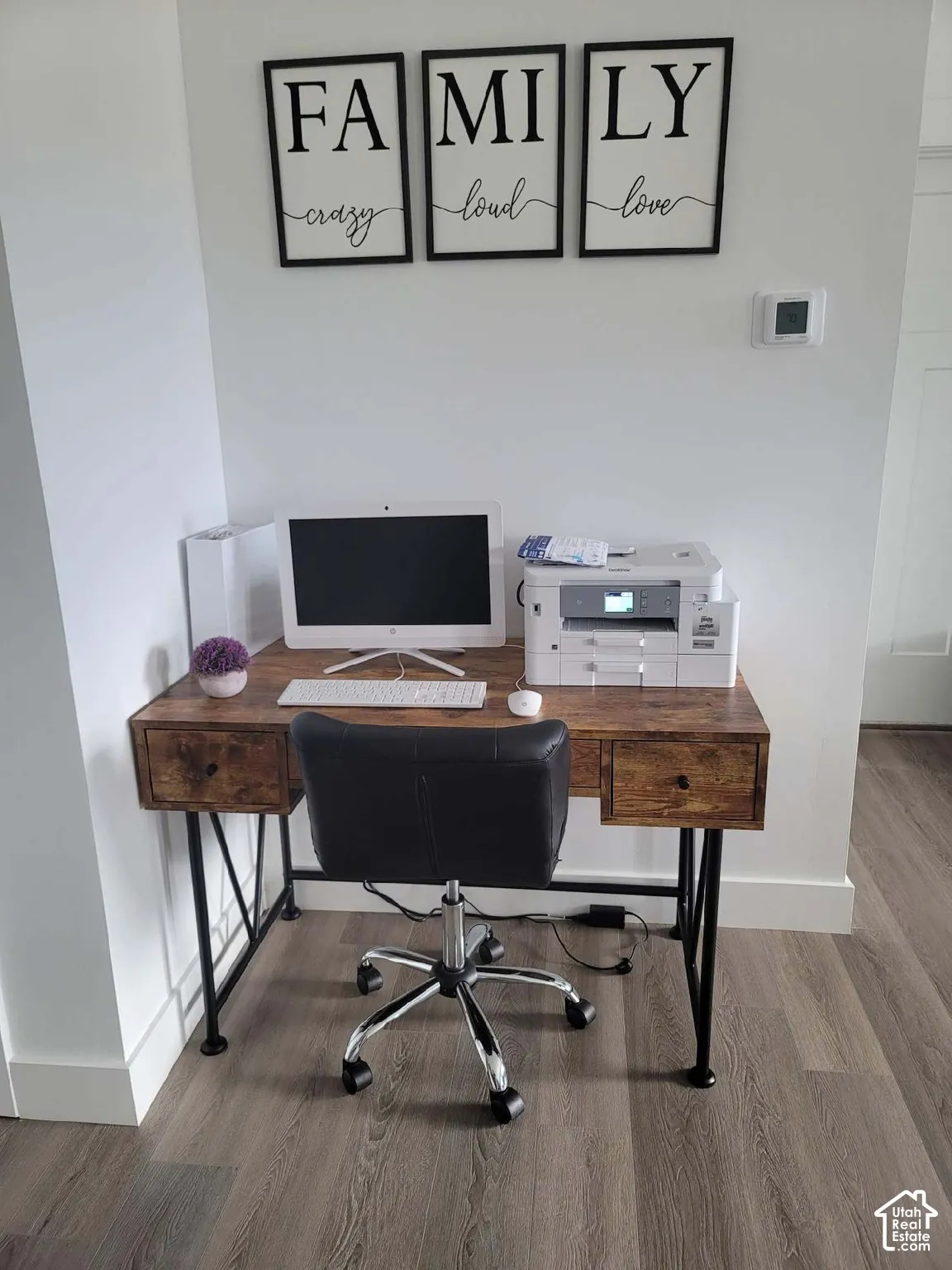 Wood-finish flooring with white baseboards, a white wall, and a visible thermostat