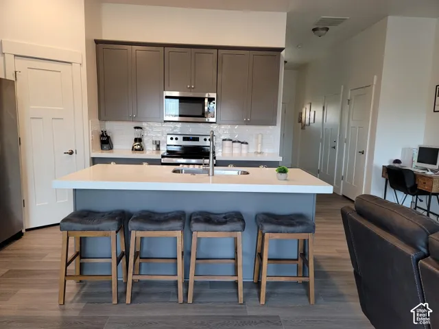 Modern kitchen featuring gray cabinetry, stainless steel appliances, white subway tile backsplash, and an island with an undermount sink