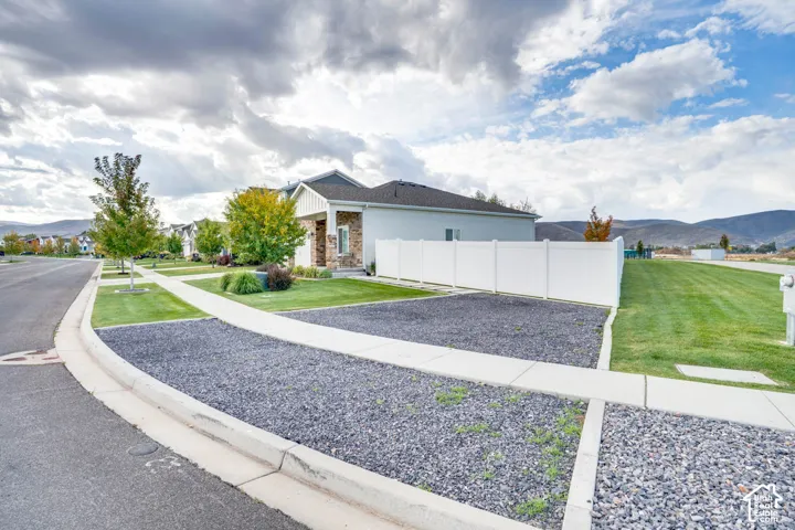 Contemporary residence featuring a covered porch with stone detailing, a white privacy fence, and a landscaped yard with mature trees