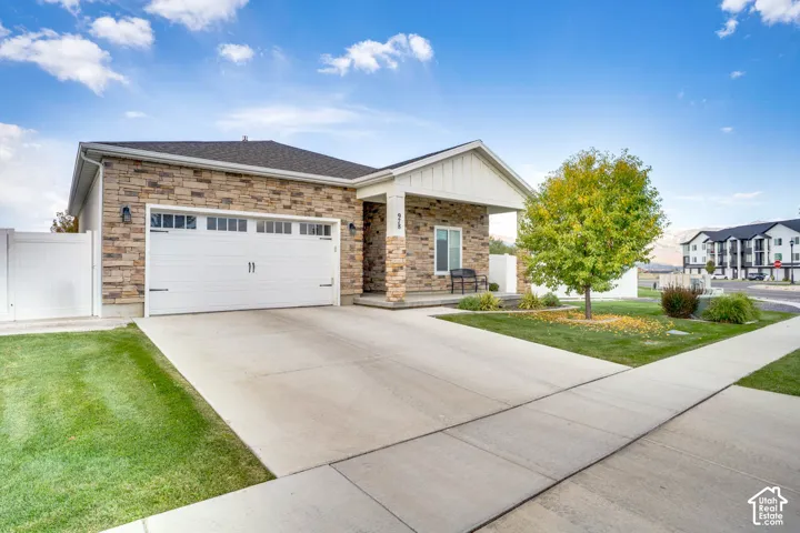 Stone veneer exterior with a white garage door, concrete driveway, covered porch, and mature landscaping