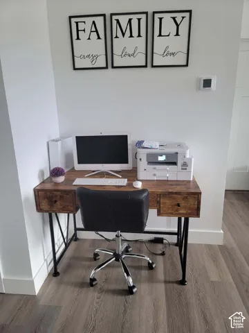 Wood-finish flooring with white baseboards, a white wall, and a visible thermostat