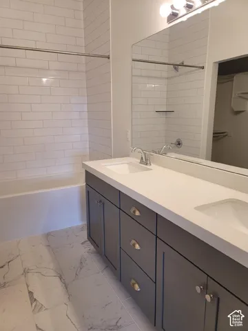 Dual vanity with gray cabinetry and white countertops, subway tile shower surround, and patterned floor tile