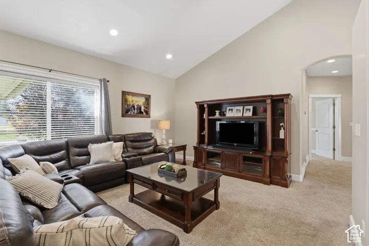 Vaulted ceiling with recessed lighting, large window with blinds, neutral wall paint, and carpeted flooring