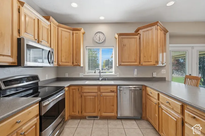 Hardwood cabinetry, stainless steel appliances, recessed lighting, tile flooring, and a window above the sink