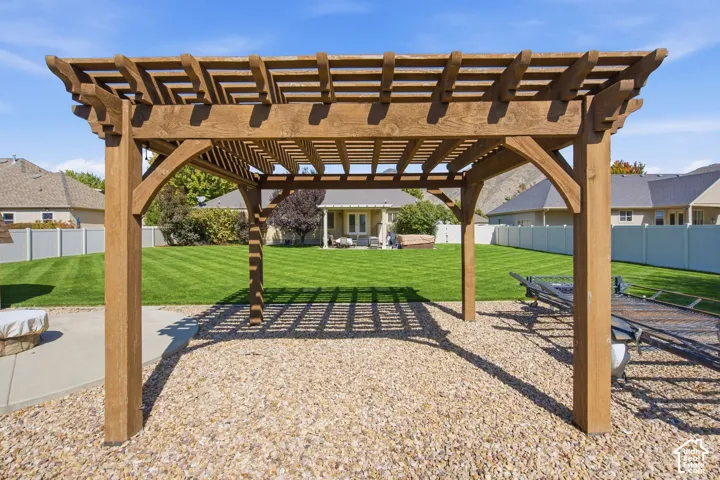 Wood pergola over a gravel patio, featuring a manicured lawn and a white privacy fence
