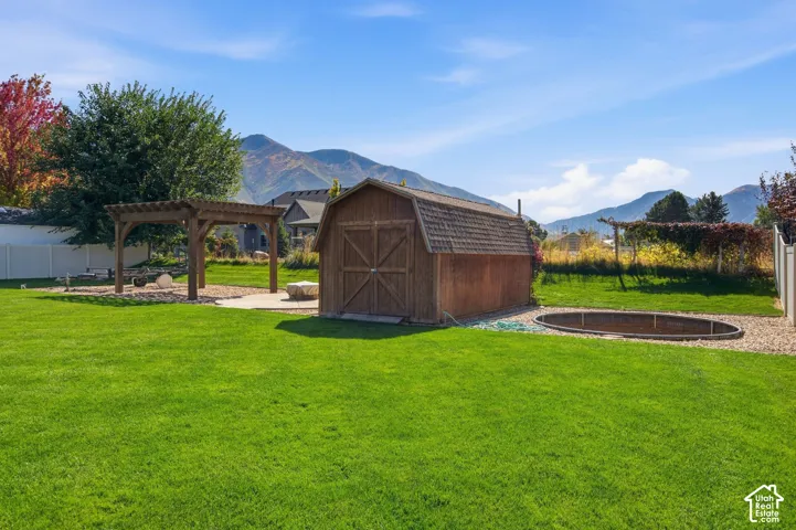 Expansive green lawn featuring a wooden pergola over a patio, a detached wooden shed, and a recessed circular structure