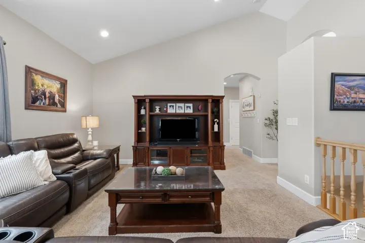 Vaulted ceiling, recessed lighting, arched doorway, light wood-finish banister, and carpet flooring