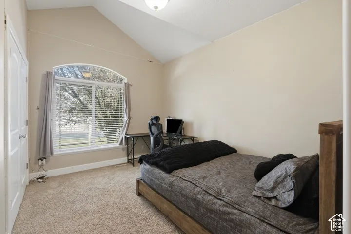 Arched window with blinds, vaulted ceiling, neutral carpet flooring, and a white interior door