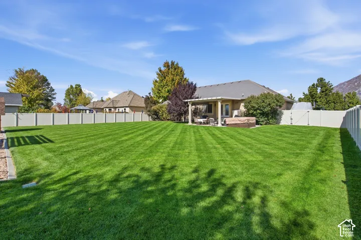 Expansive green lawn with striped mowing, fenced perimeter, covered patio, and mountain backdrop