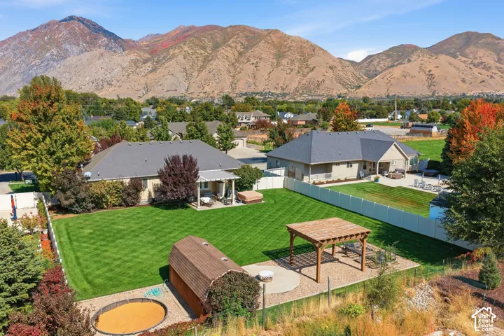 Expansive backyard featuring a manicured lawn, a wooden pergola on a gravel patio, and a storage shed