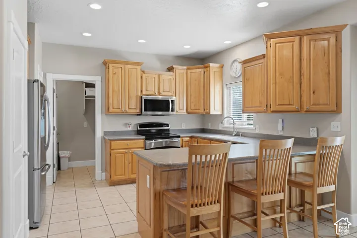 Kitchen featuring wood cabinetry, stainless steel appliances, recessed lighting, and a kitchen island with counter seating