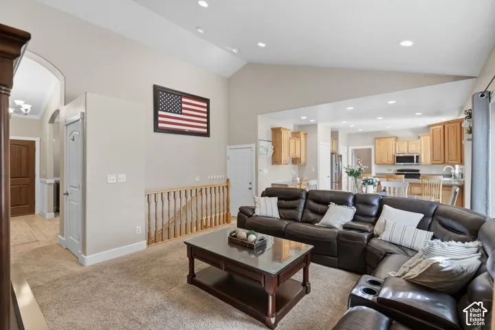 Vaulted ceiling, recessed lighting, wood-finish railing, archway entry, and a kitchen with wood-finish cabinetry