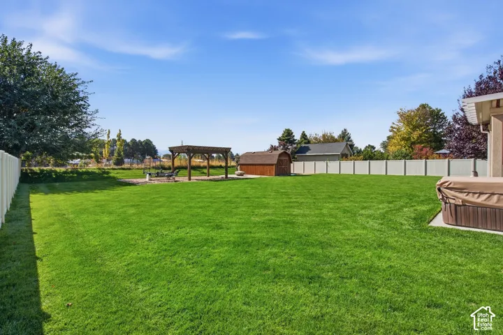 Expansive lawn area featuring a pergola-covered patio, an unattached storage shed, and a privacy fence