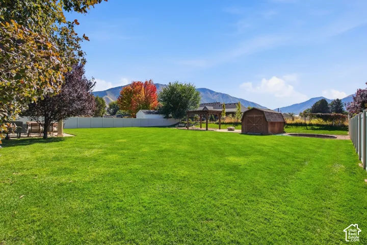 Expansive grassy yard with a white privacy fence, wood-finish shed, and a structured pergola