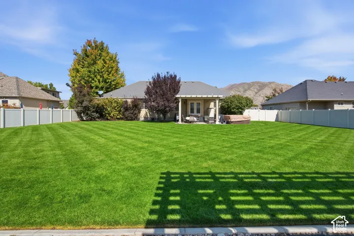 Expansive backyard featuring a lush lawn, privacy fencing, and a covered patio area