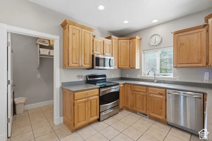 Kitchen featuring wood cabinetry, stainless steel appliances, tiled flooring, and a window with blinds