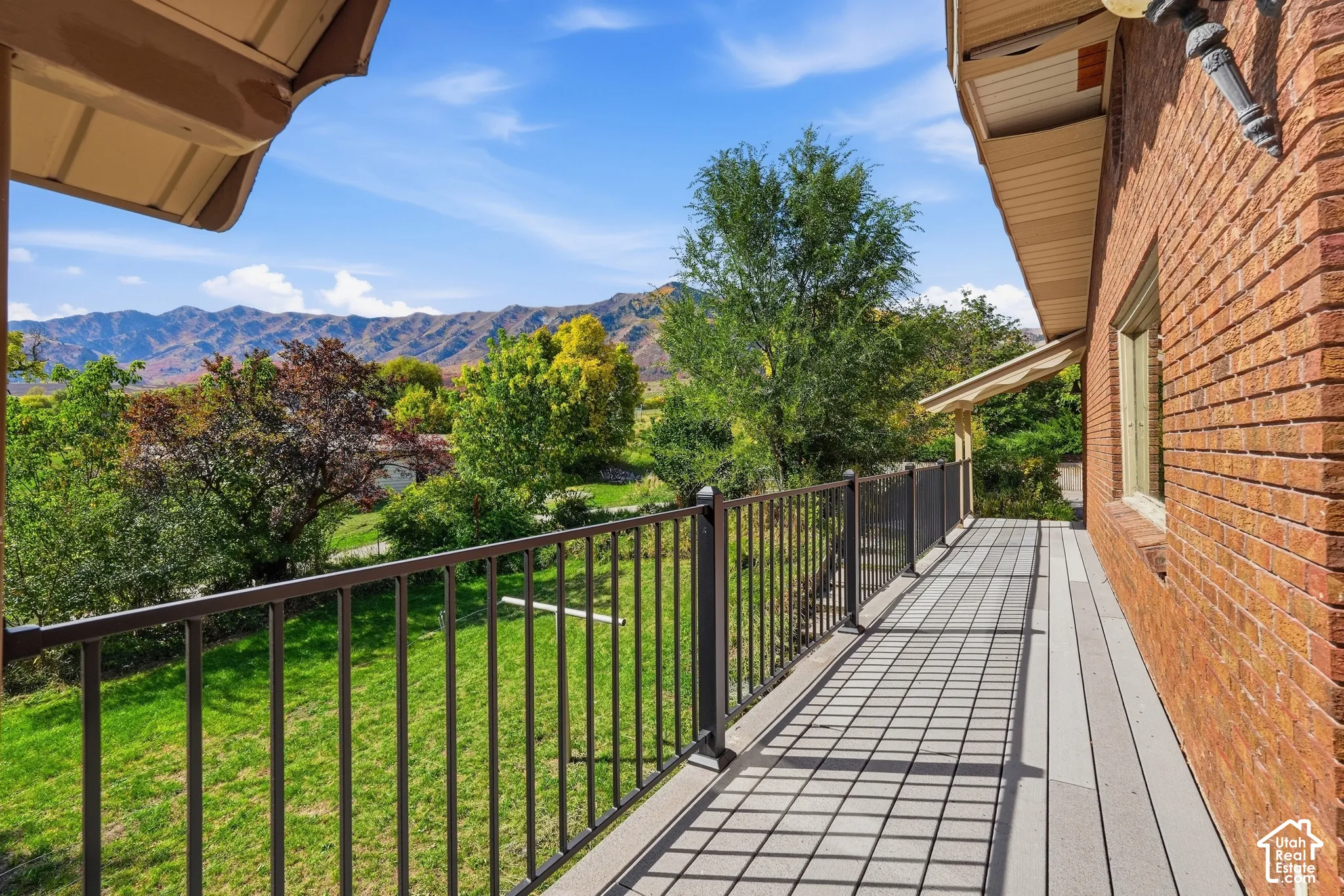 Expansive outdoor deck with composite decking and metal railing, featuring a brick exterior and a clear mountain backdrop