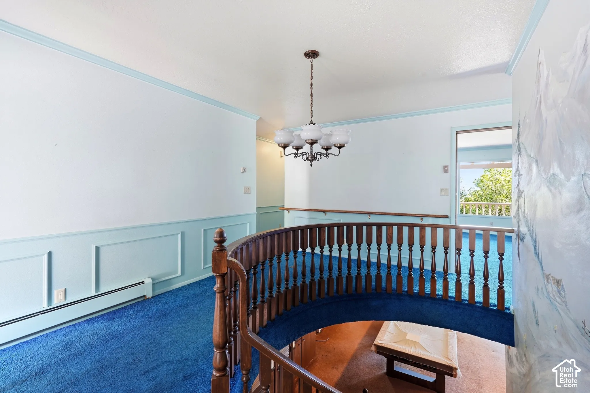 Upper landing featuring a curved wood banister, blue carpeting, and a chandelier