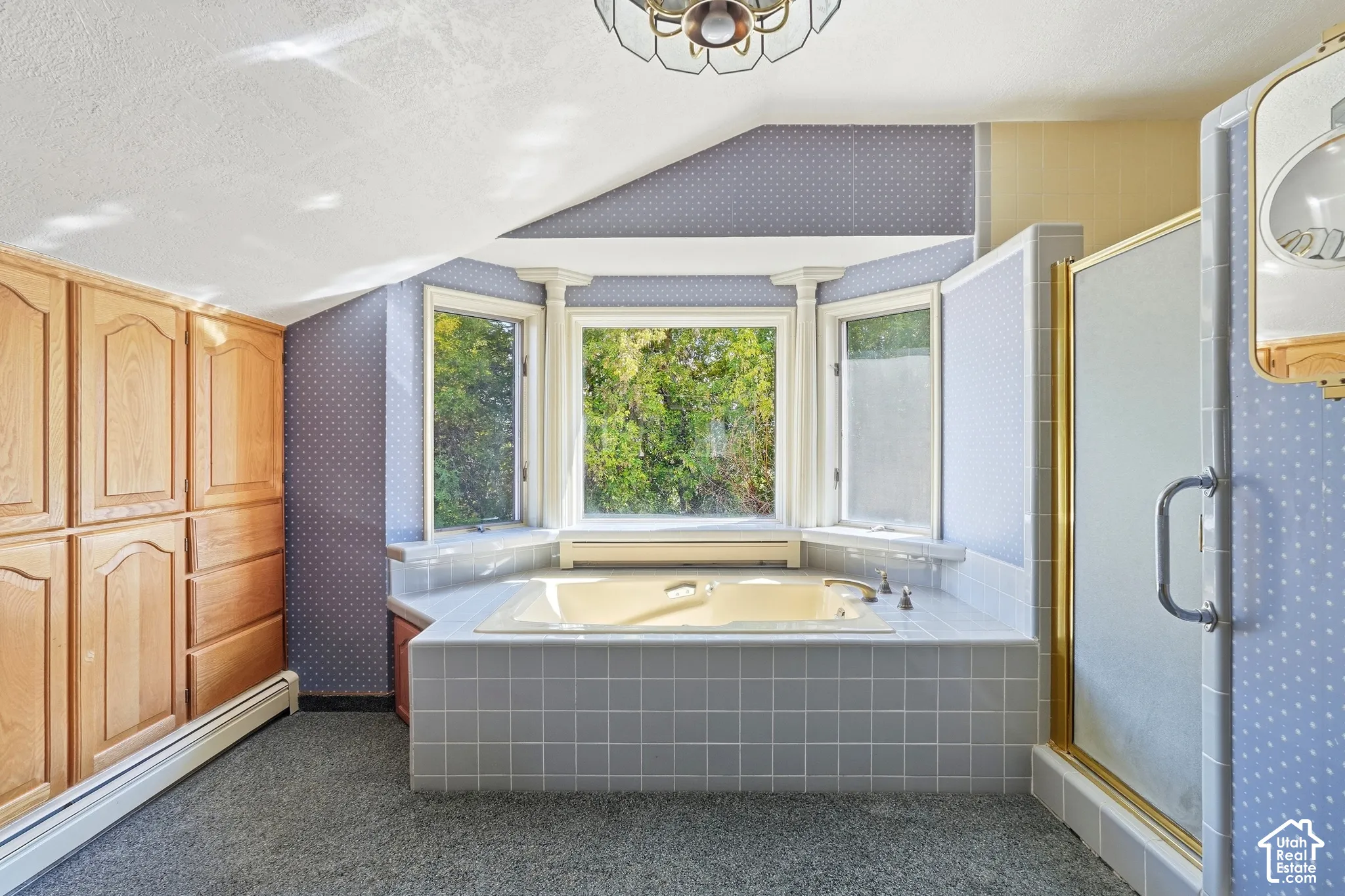 Built-in storage cabinetry, bay window, tiled soaking tub, tiled shower with gold-toned frame, and ceiling-mounted light fixture
