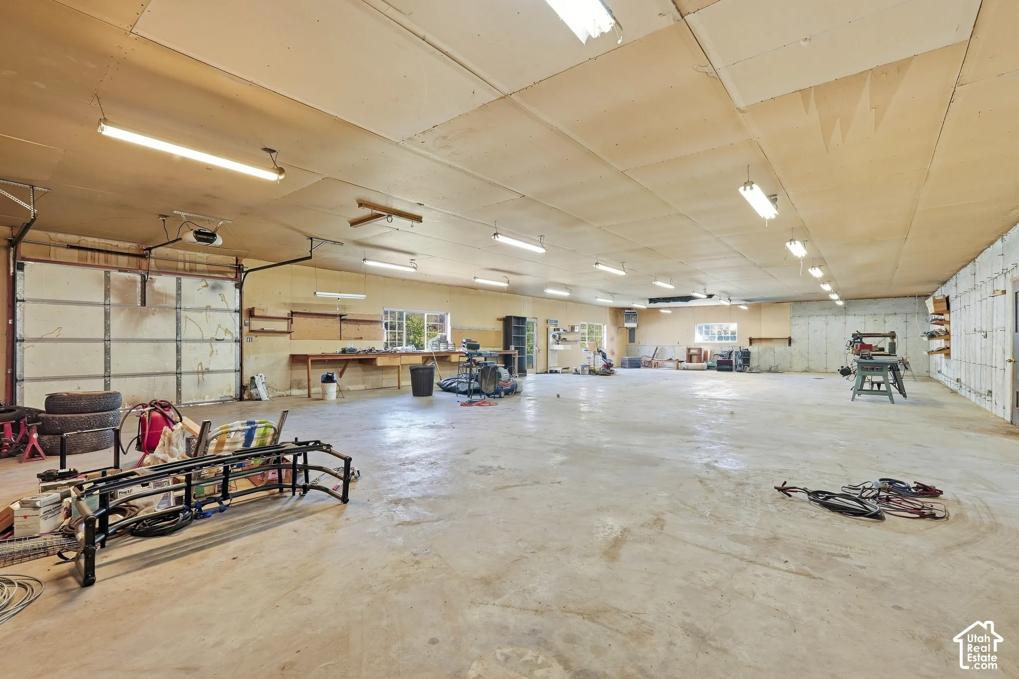 Spacious interior featuring a large garage door, concrete flooring, exposed ceiling, built-in shelving, and multiple windows
