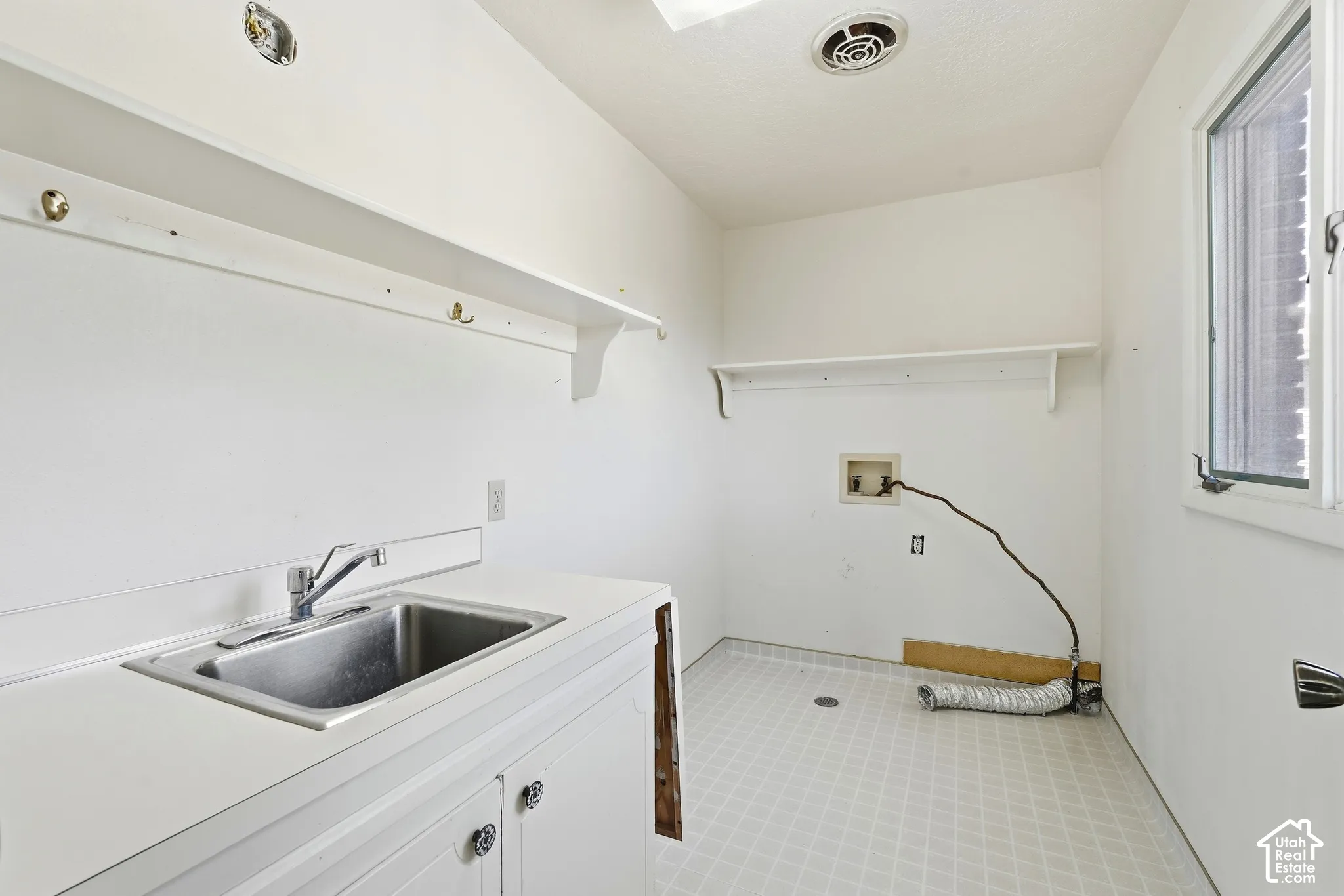 Utility room featuring a built-in sink with cabinetry, overhead shelving, and window