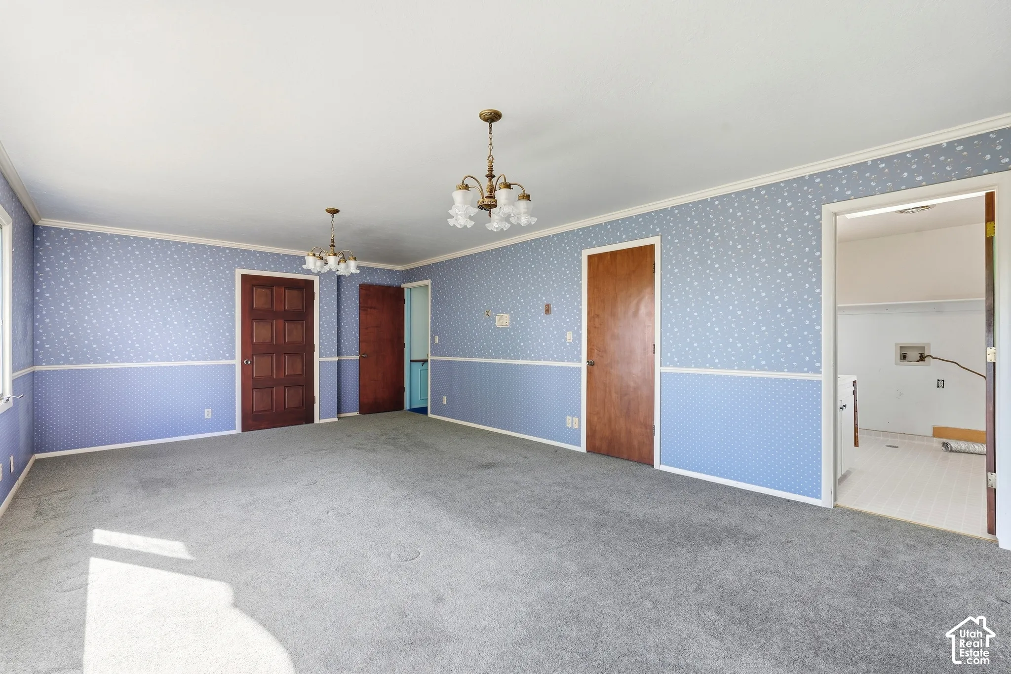 Spacious room with patterned wallpaper, two brass chandeliers, and multiple wooden panel doors