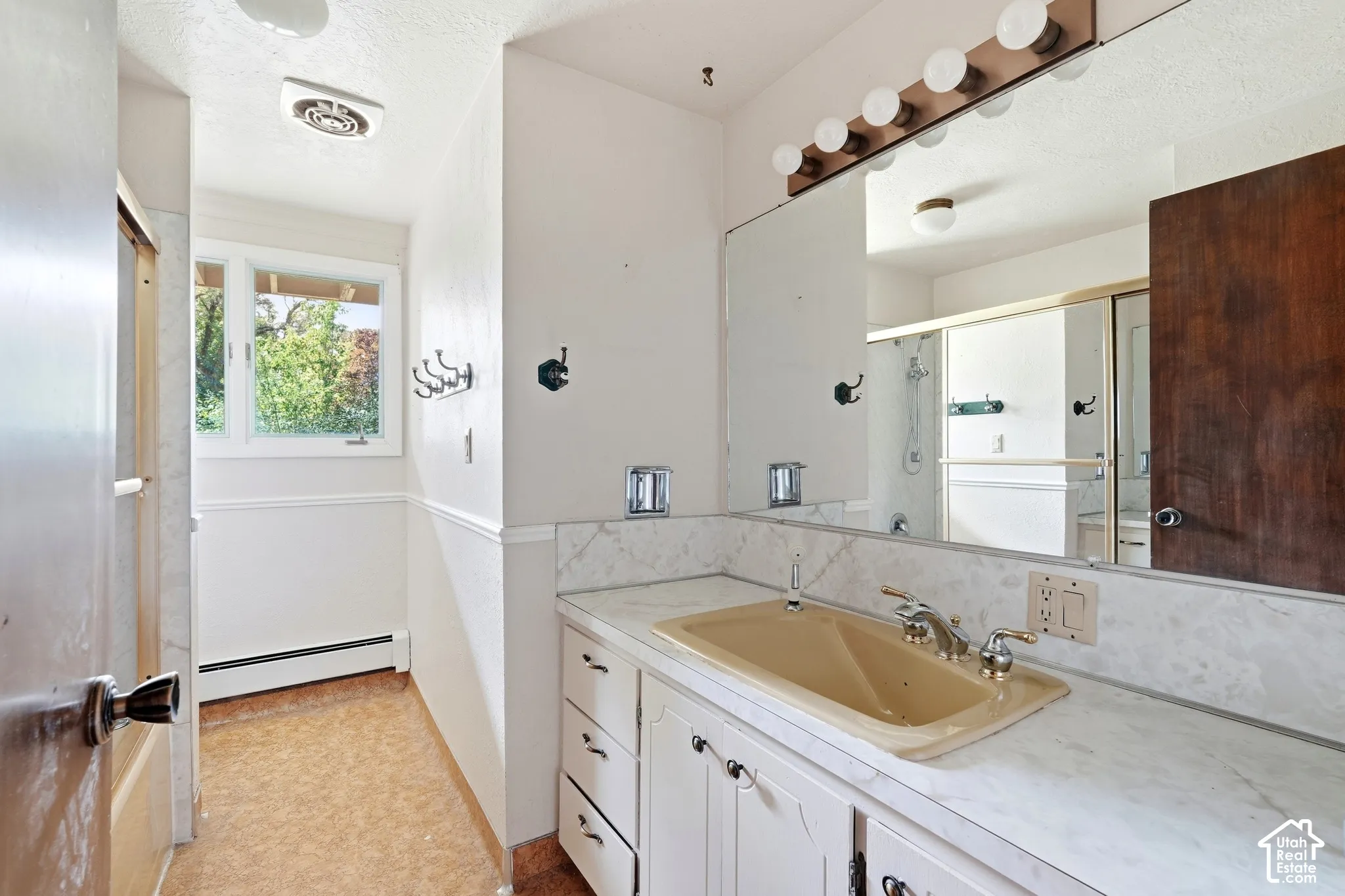 Vanity with integrated sink, full-width mirror with overhead lighting, white cabinetry with decorative pulls, and a window with exterior views