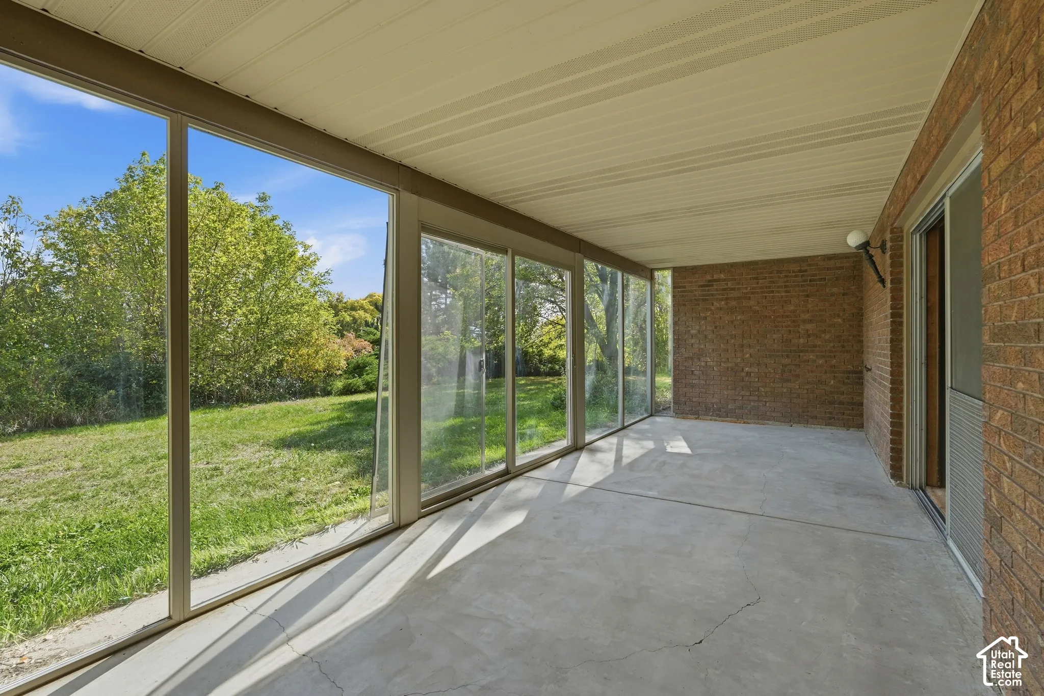 Covered patio with a concrete surface, brick exterior wall, and full-height glass panels