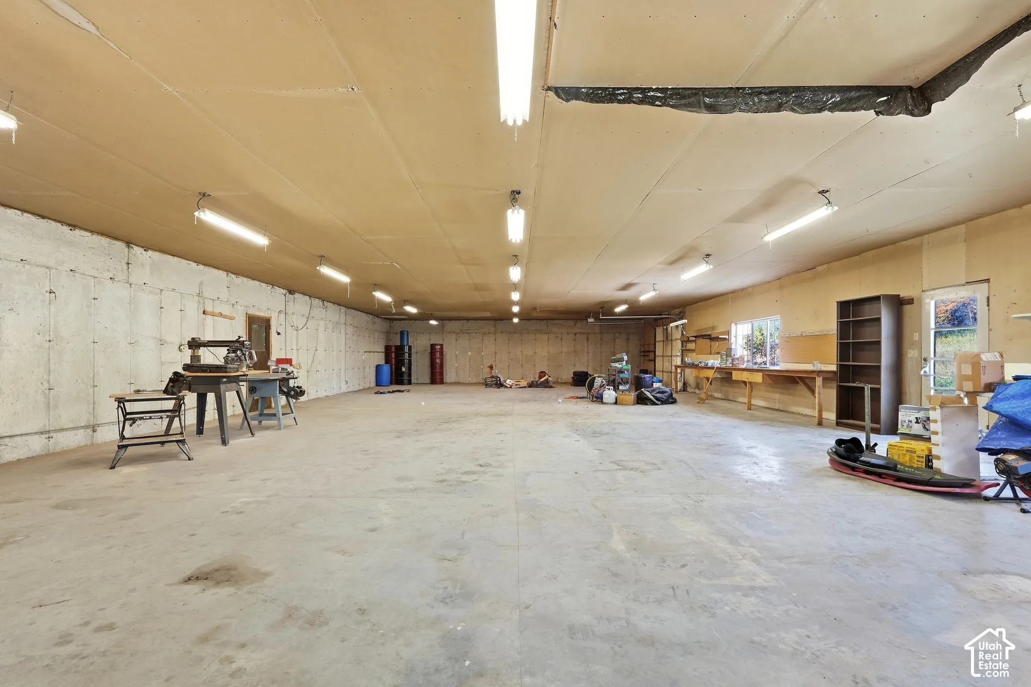 Expansive concrete floor, concrete walls, multiple fluorescent light fixtures, and a workbench with shelving