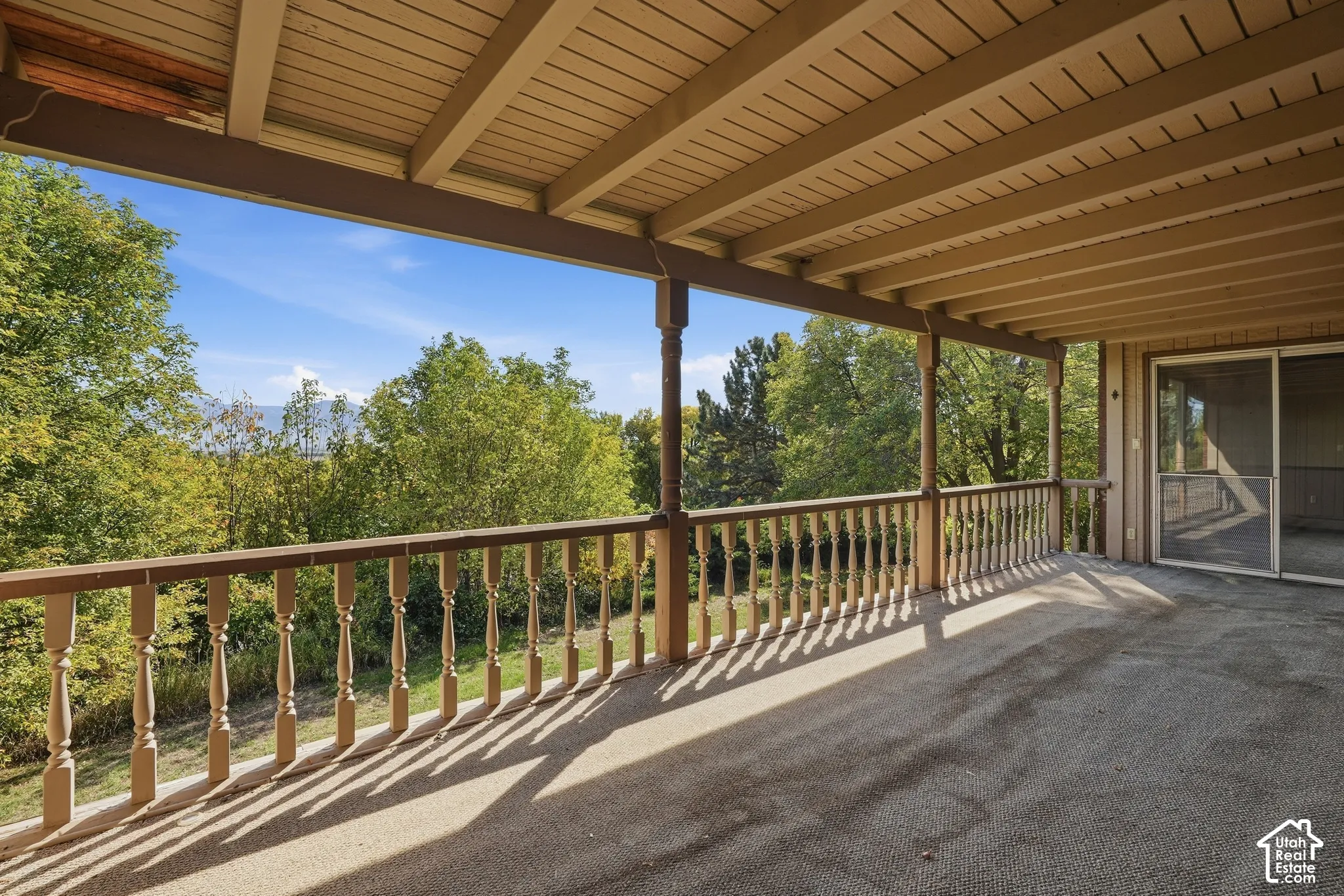 Expansive covered deck featuring a textured surface, classic baluster railings, and a sliding glass door entry