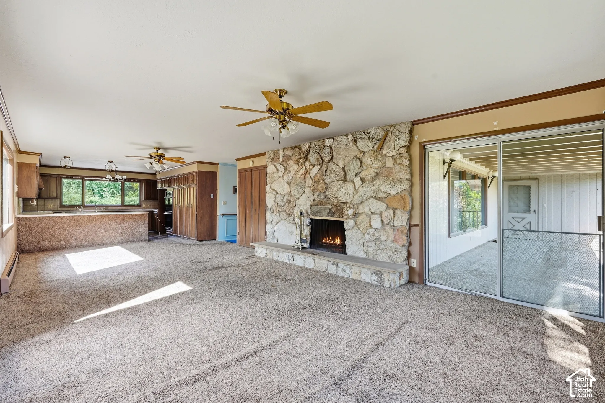 Stone-faced fireplace with a hearth, sliding glass door, overhead ceiling fans, and an integrated kitchen bar area with wood cabinetry