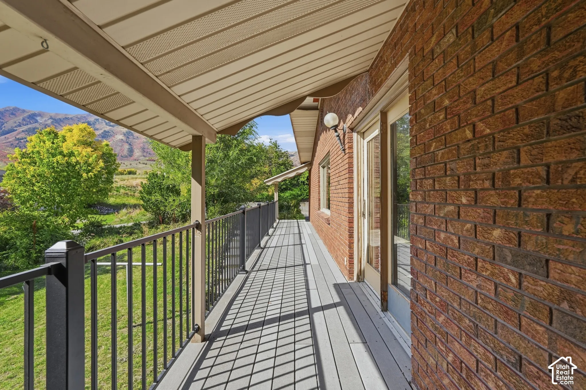 Covered outdoor deck with composite decking, black metal railing, and a brick exterior wall