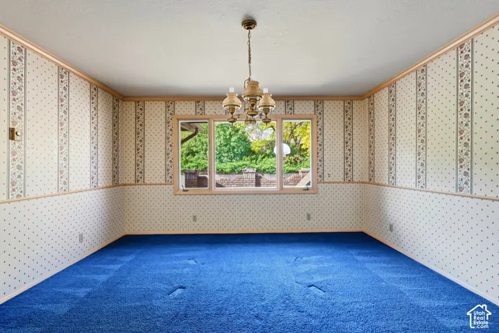 Expansive room with patterned wallpaper, wood-tone trim, a central multi-bulb chandelier, and a large picture window