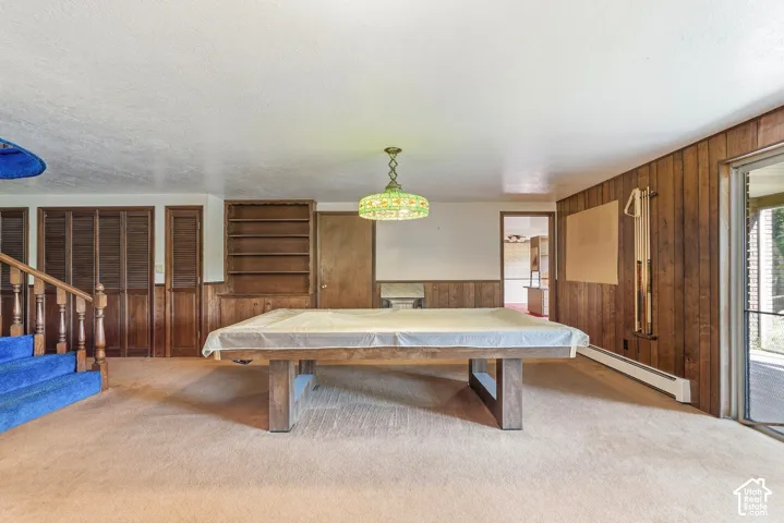 Spacious recreation room featuring wood paneling, built-in shelving, a wood staircase with blue carpeting, and a glass-paneled exterior door