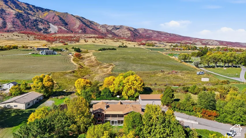 Expansive property featuring a brown roof, surrounding mature trees, a driveway, and distant mountainous terrain